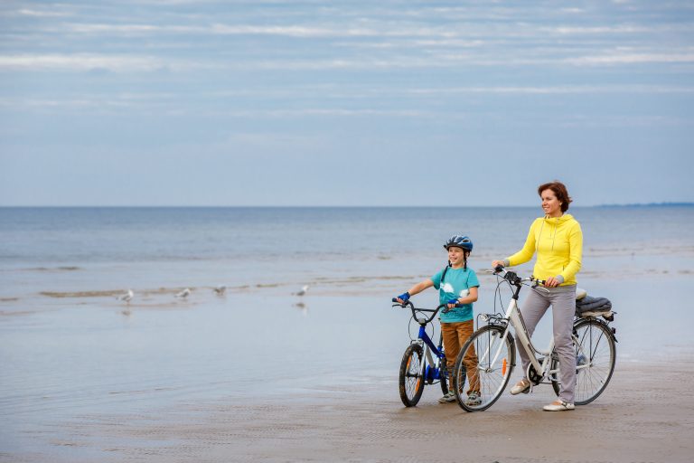 Aktiviteetit, Jurmala, pyöräily Äiti ja poika hymyilevät rannalla pyörien kanssa seisten.